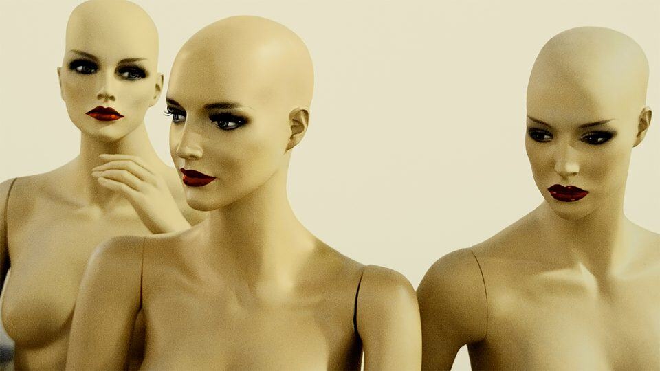 Bald mannequins with striking makeup, including bold red lips and dark eye makeup, displayed in a showroom for fashion, beauty, or retail branding purposes.